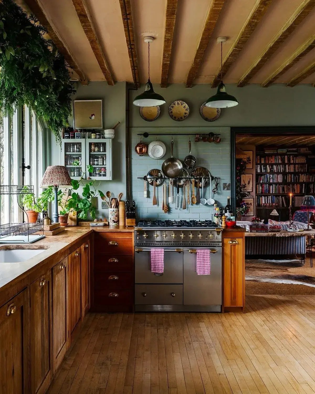 Sage green kitchen with hanging copper and steel pans above a range cooker