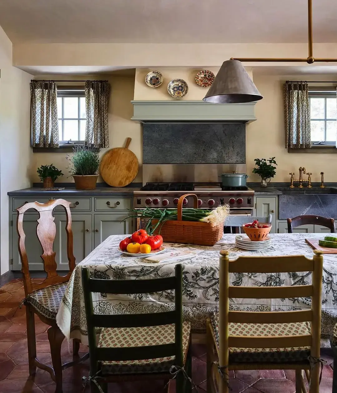 Sage kitchen diner with terracotta floor, range cooker and mismatched chairs