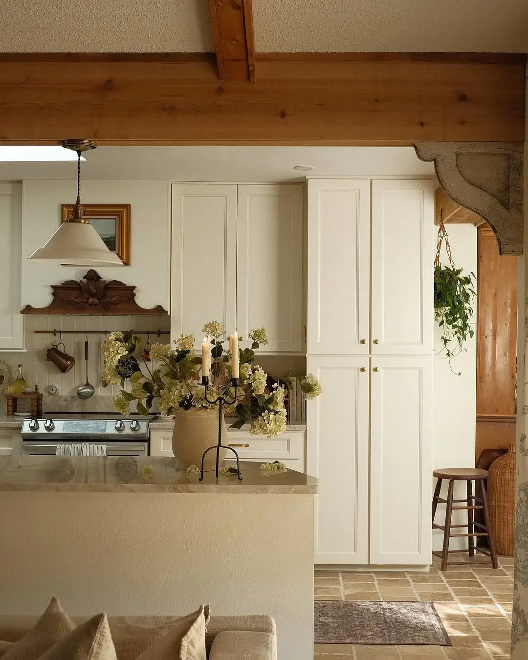 White kitchen with a single oak beam, stone corbel and hydrangeas on the island