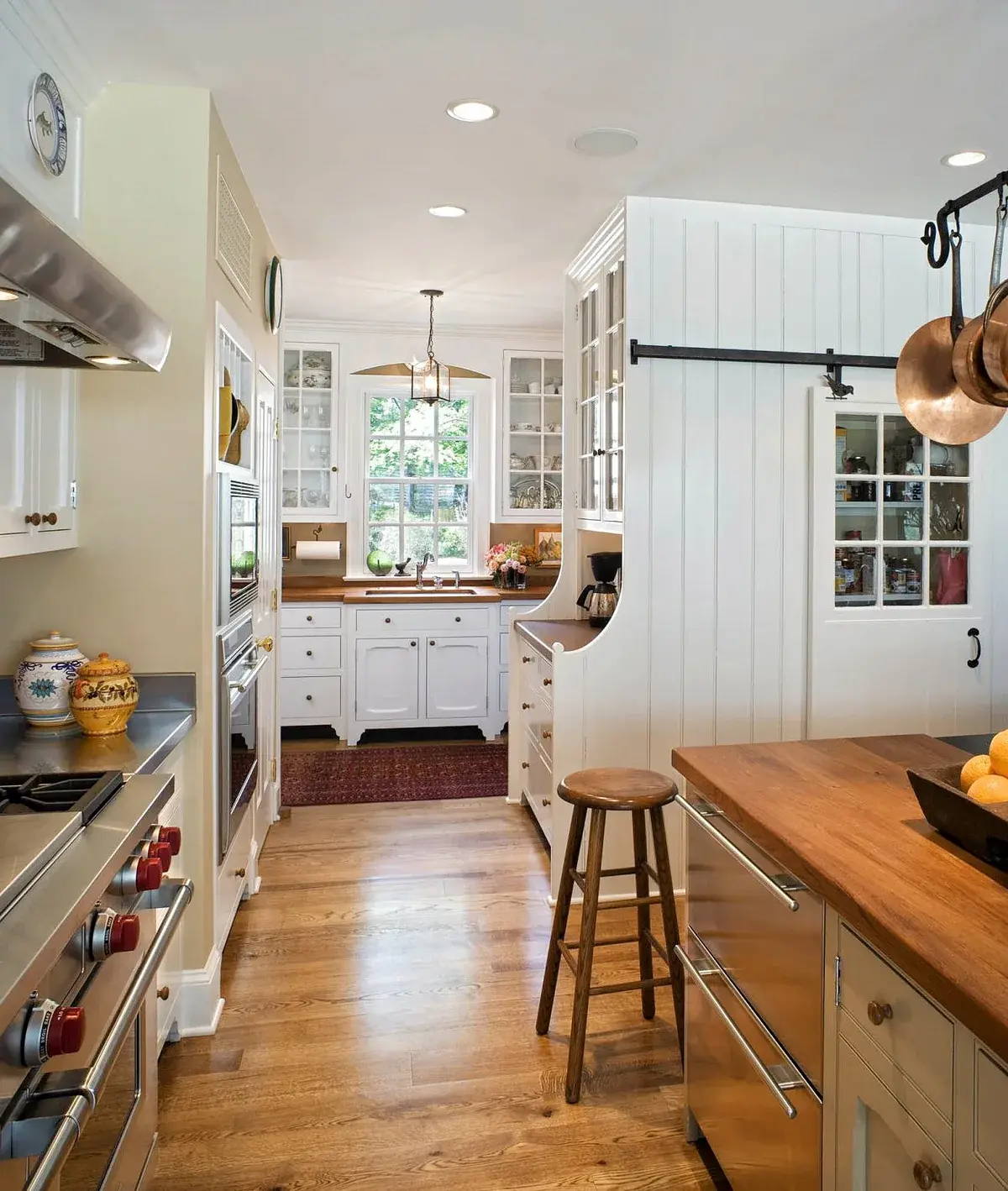 Galley kitchen with a sliding barn door pantry and copper pans overhead