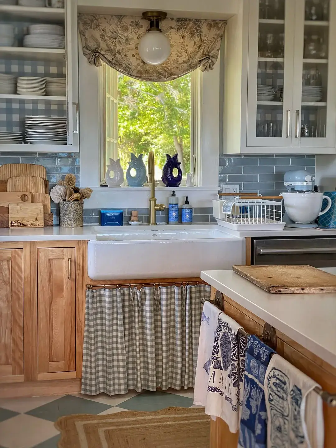 White Belfast sink with a gingham curtain below, brass tap and blue tiled wall