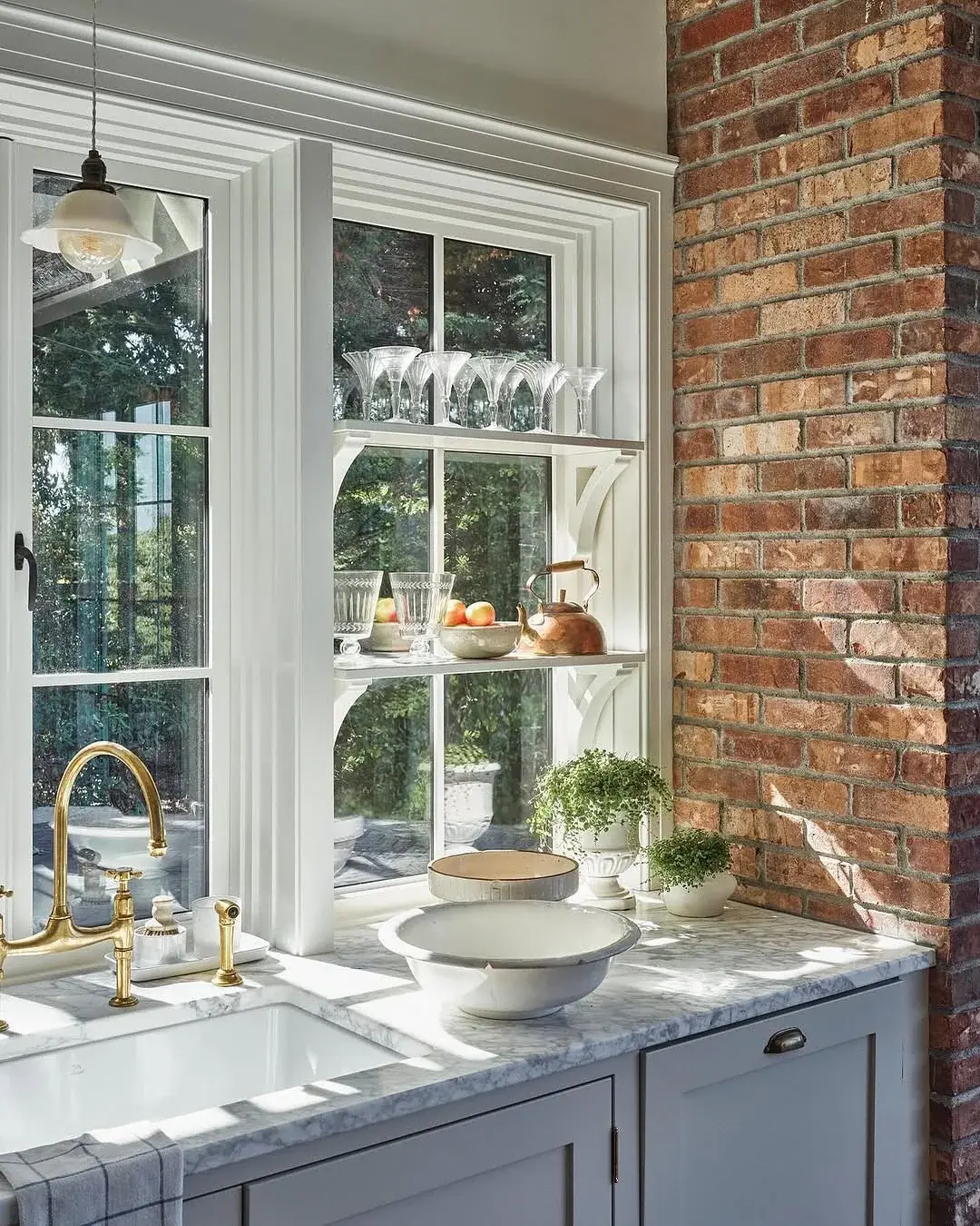 Grey kitchen with a marble top, brass bridge tap and glassware shelved across the window