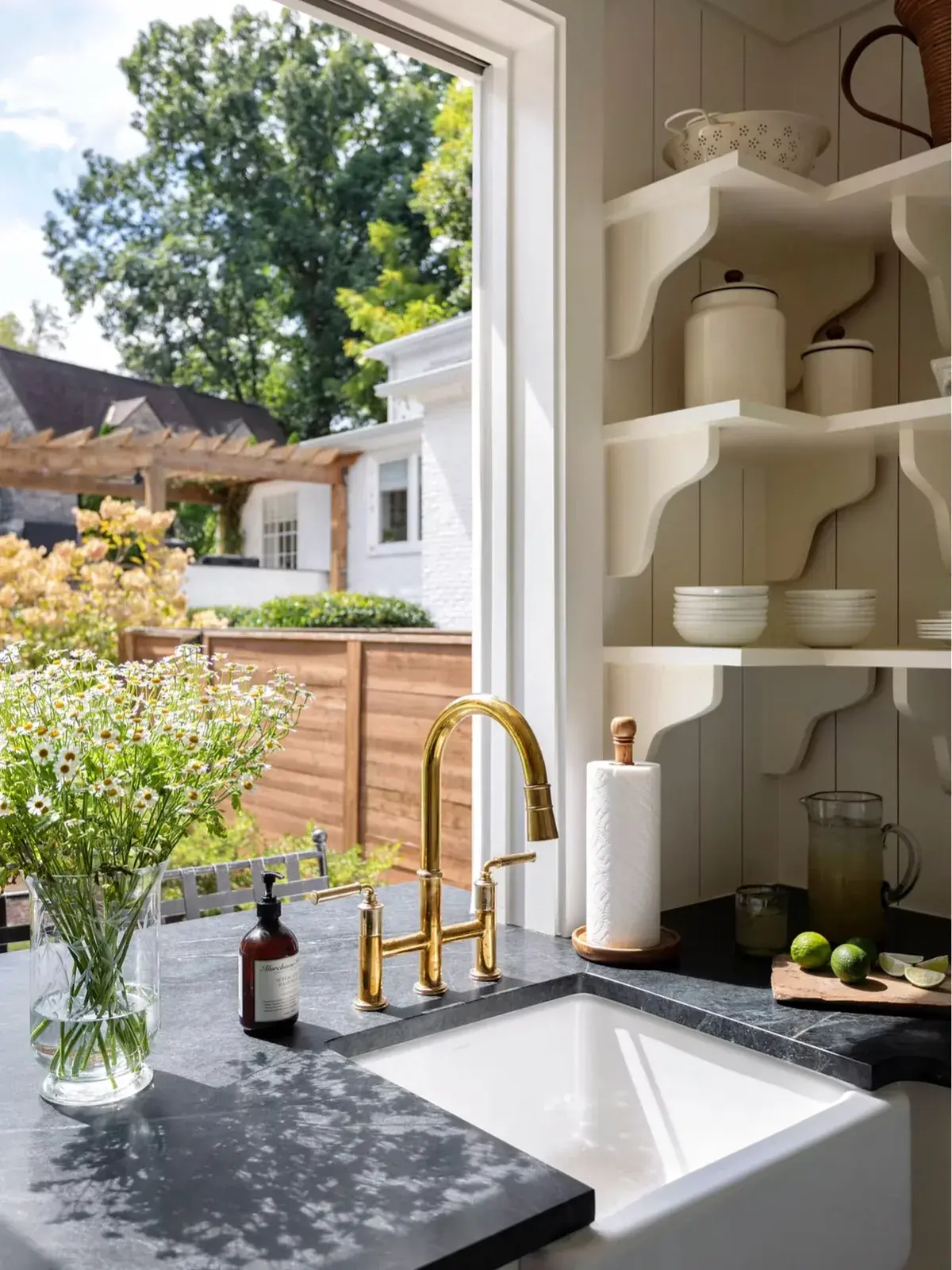 White farmhouse sink in dark stone with a brass bridge tap and open crockery shelves