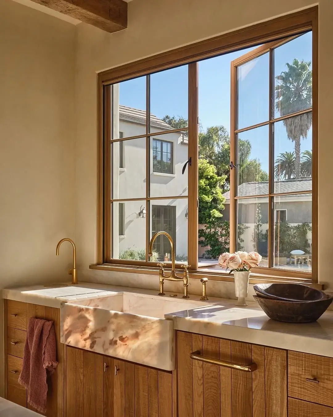 Pink veined stone apron sink with matching top, oak cabinets and brass taps