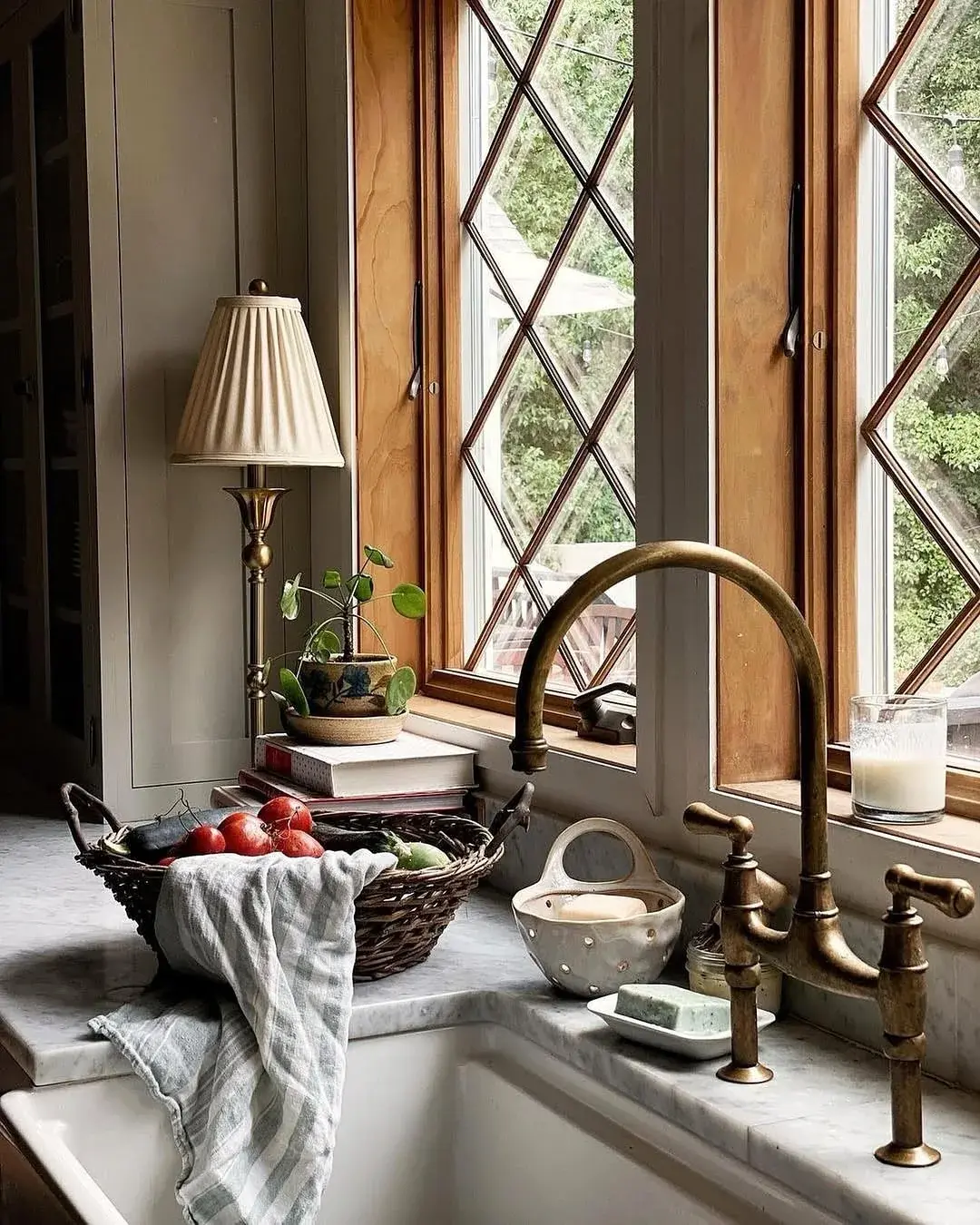 Close view of a white Belfast bowl with an aged brass bridge tap under diamond leaded windows