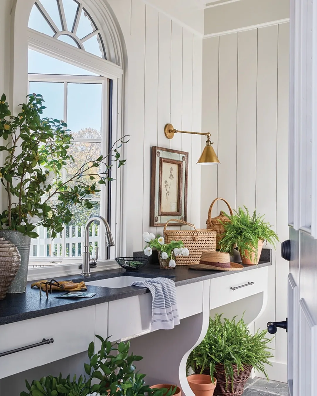 Utility sink with arched window, shiplap walls and plants on a dark stone top