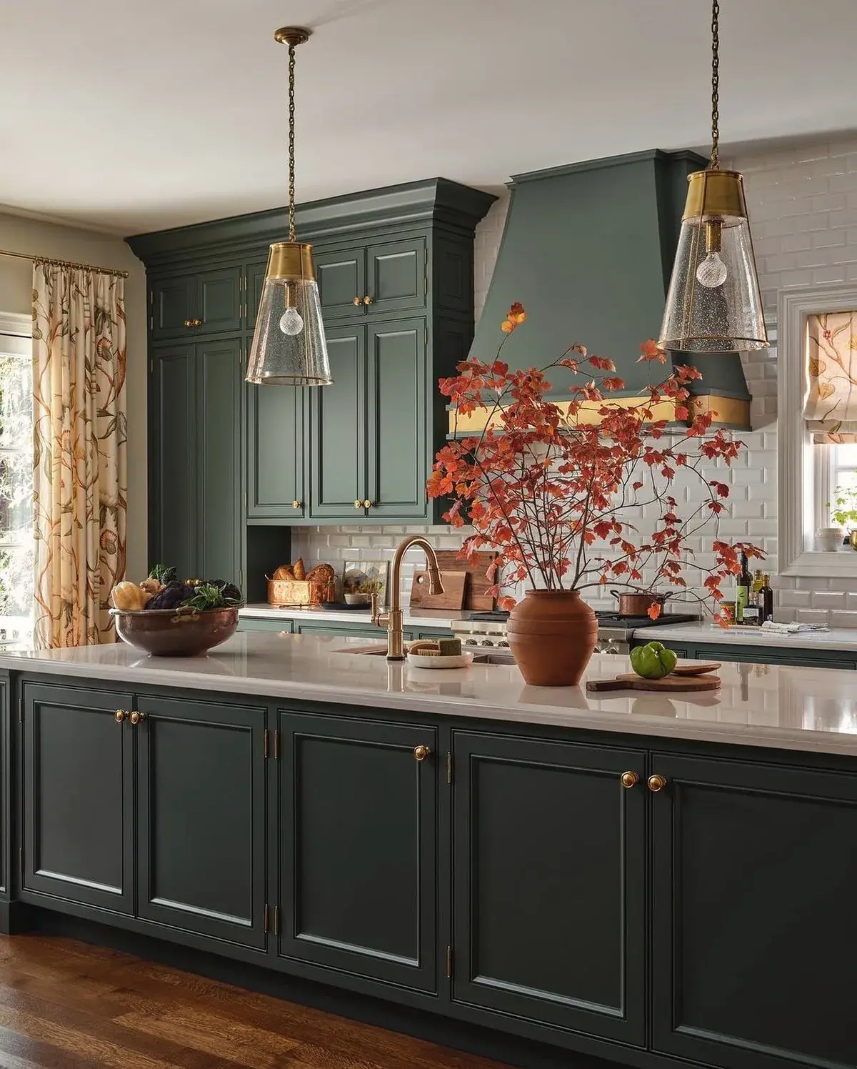 Deep green kitchen with brass knobs, white subway tile and seeded glass pendants