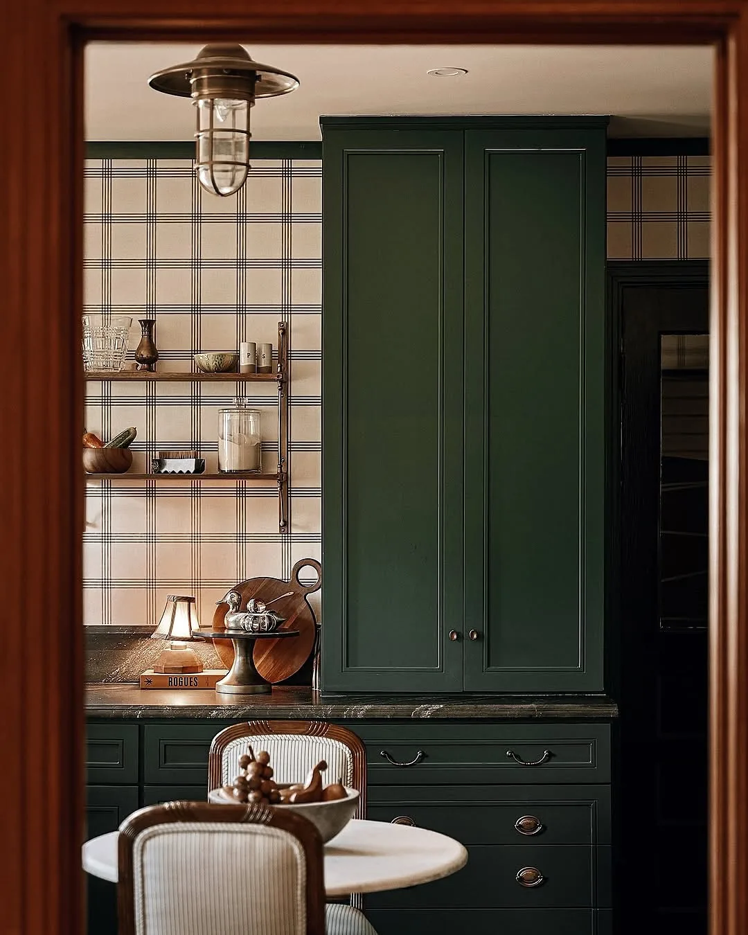 Tall forest green cupboard beside plaid wallpaper with open timber shelves