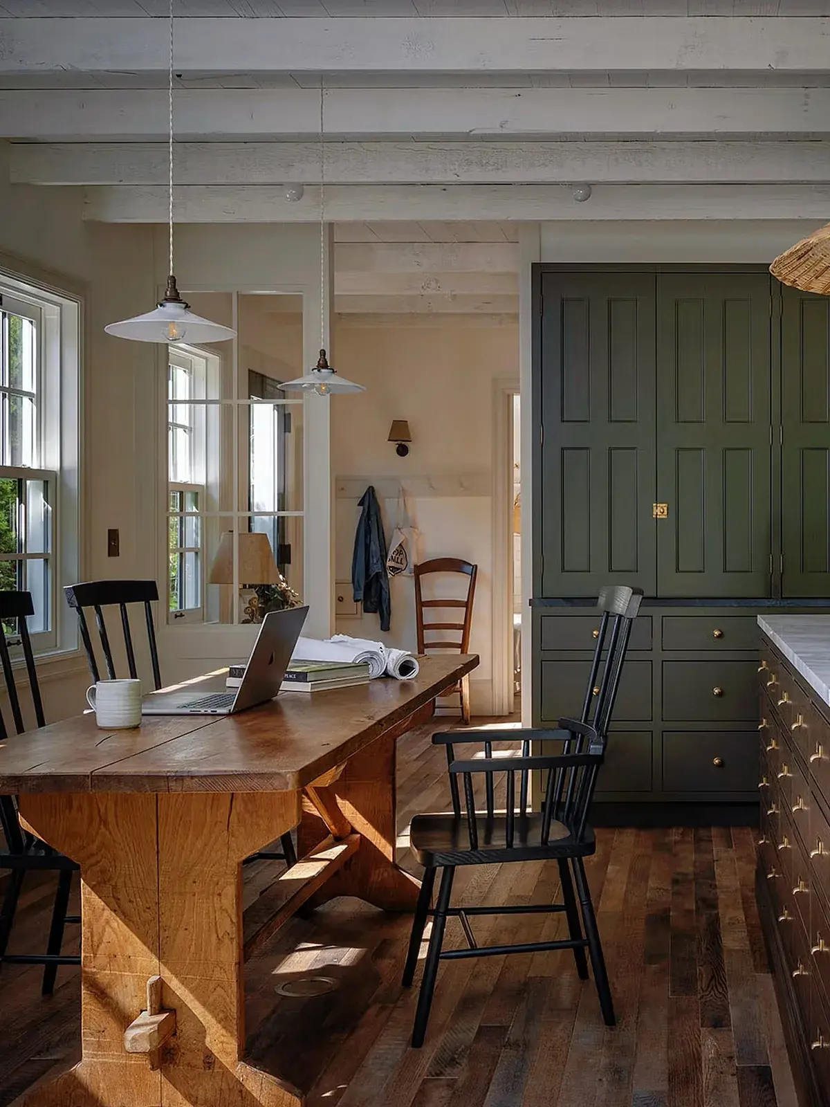Olive green pantry cupboards beside a timber trestle table with black chairs