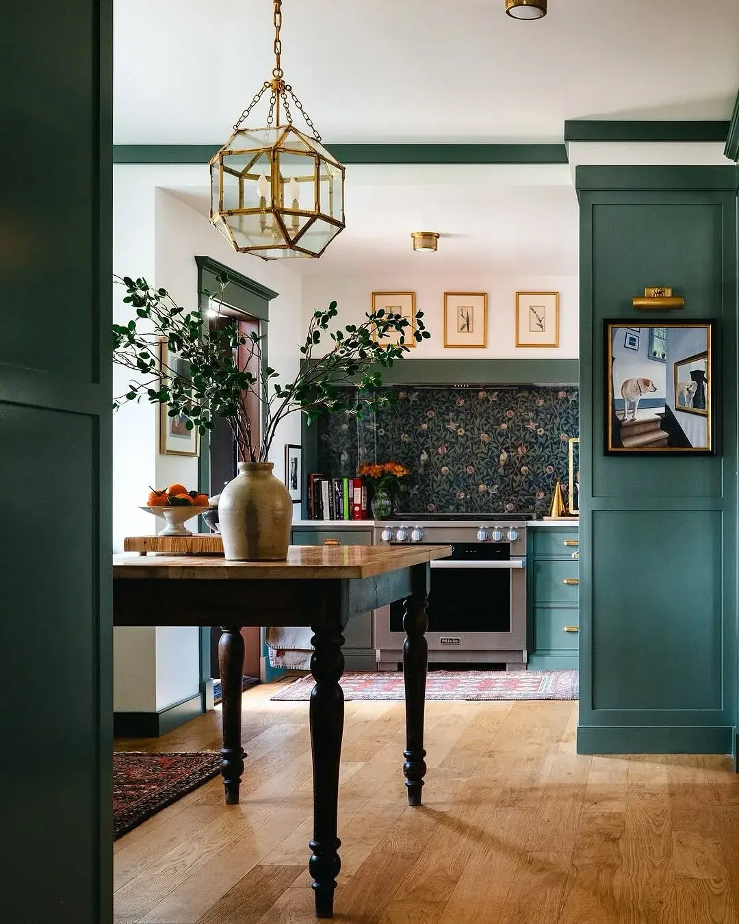 View through green panelled doorway to a range wall with floral backsplash and brass lantern