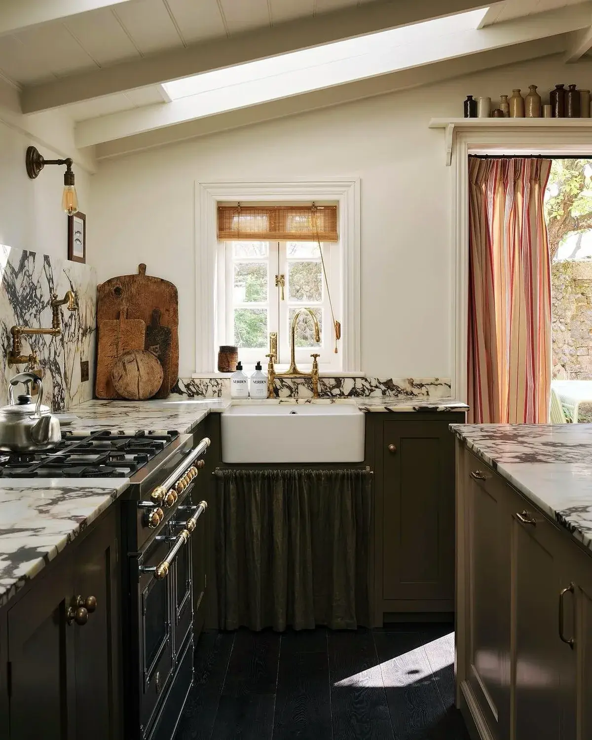 Compact olive kitchen with veined marble, skirted sink and striped curtain