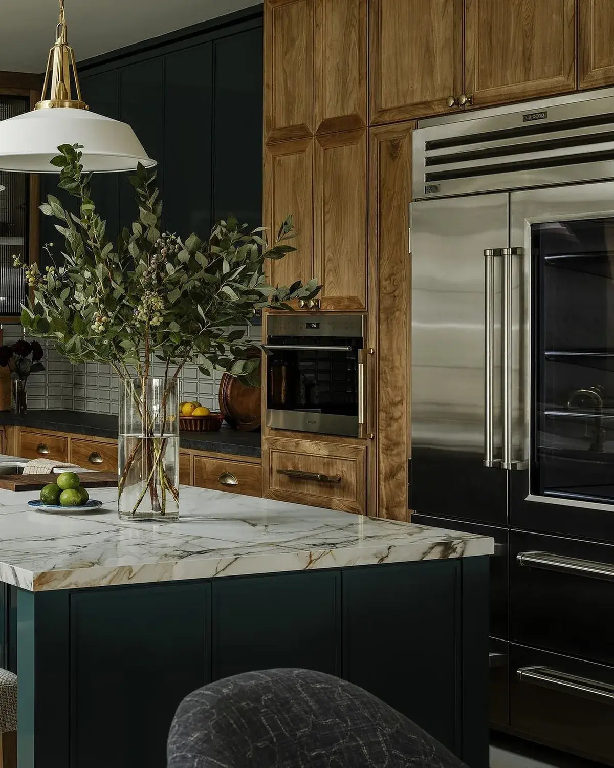 Dark green island with marble top beside an oak tower housing a steel fridge