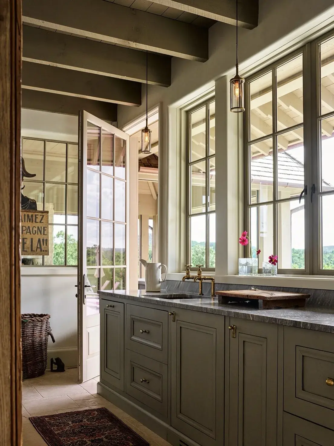 Pale sage cabinets under tall windows with a brass bridge tap and dark stone