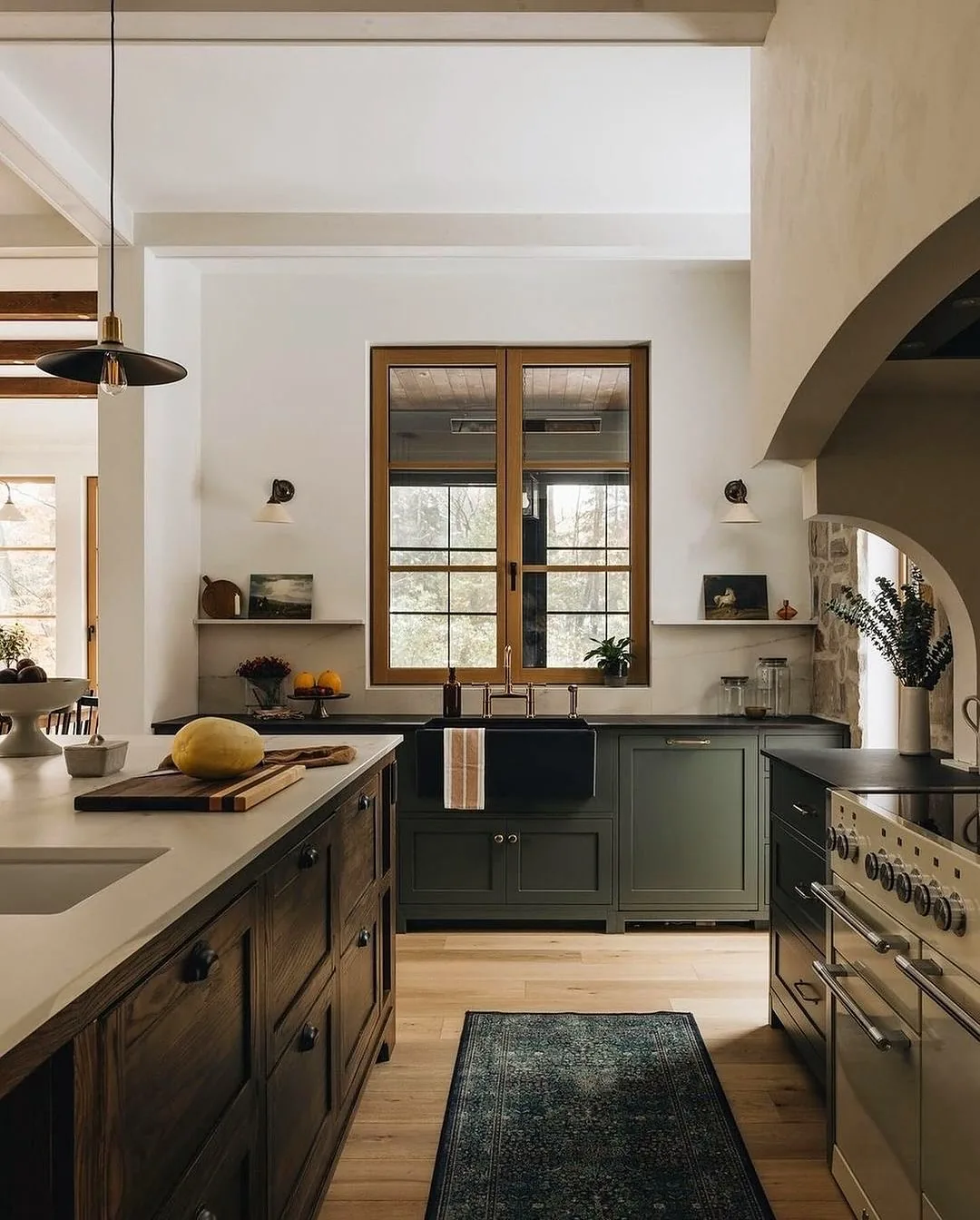 Olive kitchen with timber windows, black sink, plaster arch and wall lights