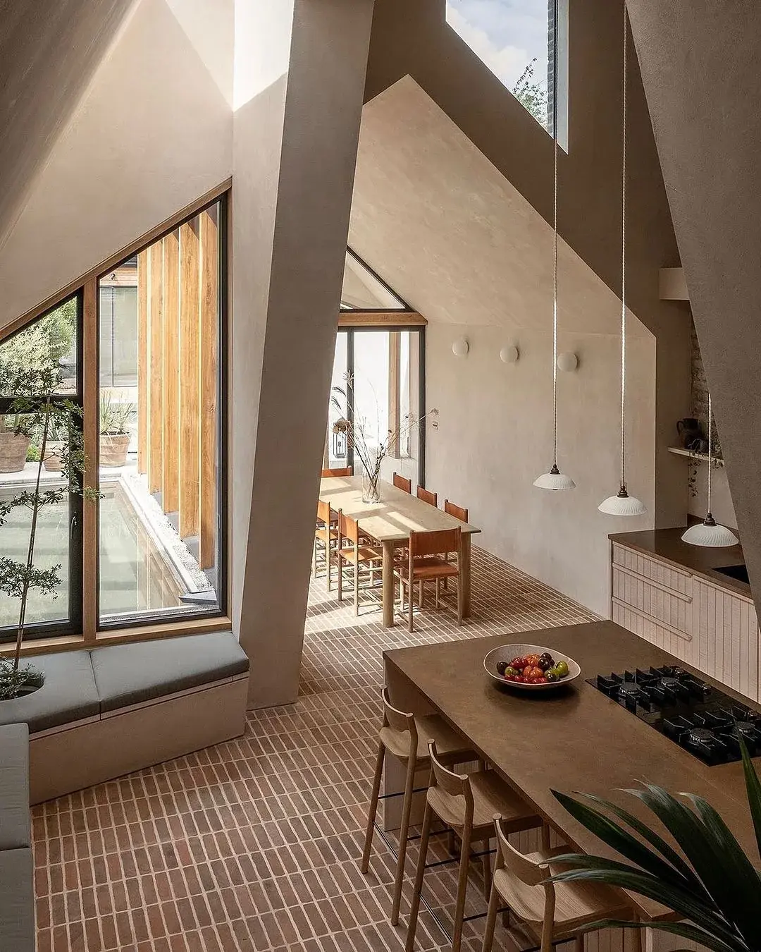 Vaulted plaster kitchen with narrow brick tile floor, island hob and oak dining set