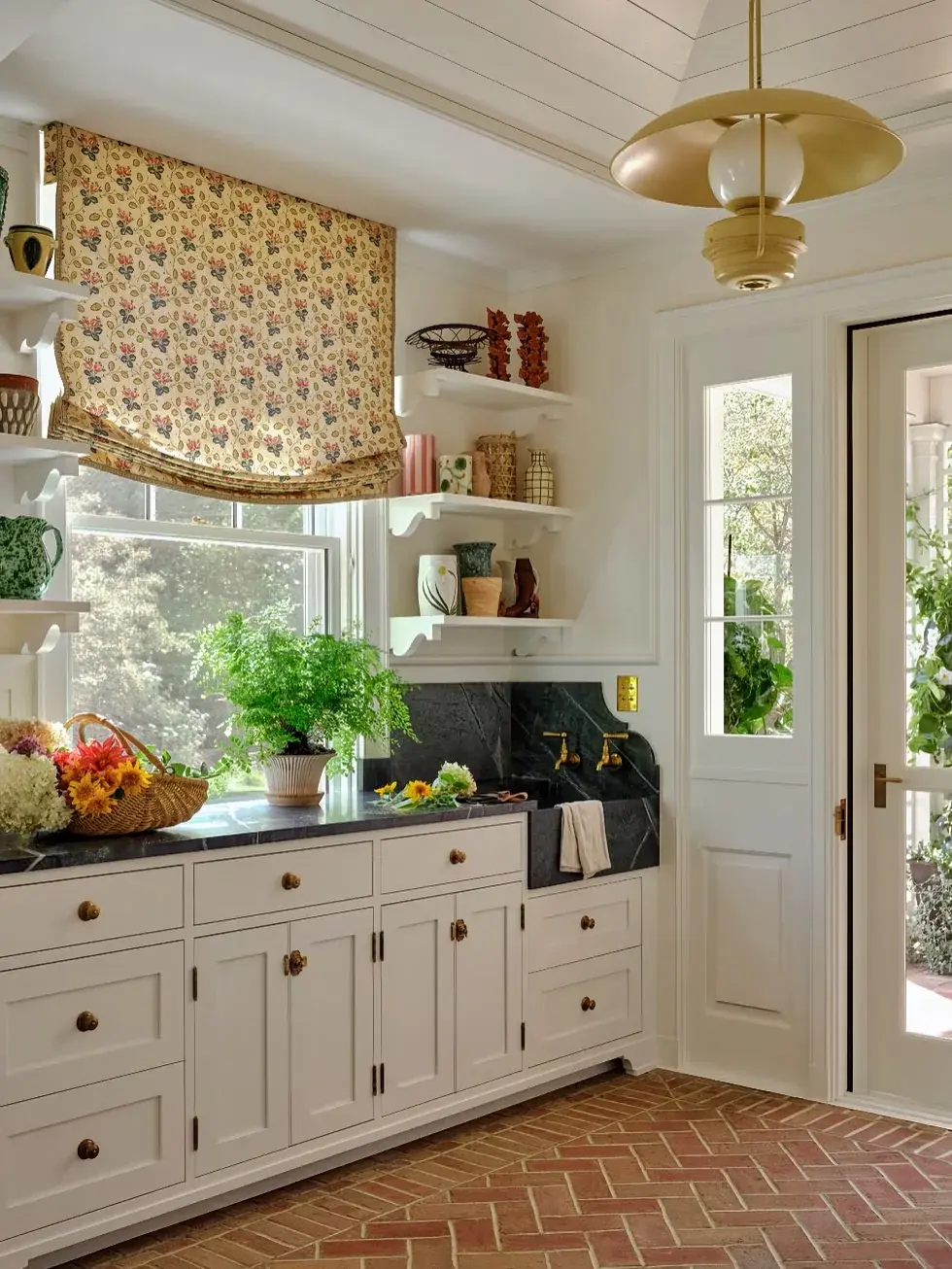 Cottage kitchen corner with herringbone brick floor, white units and floral blind