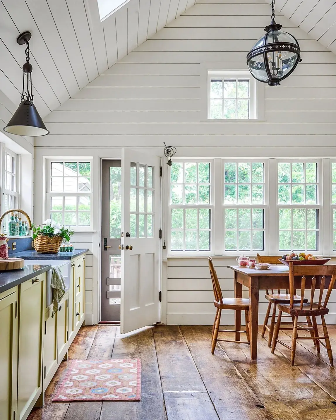 Vaulted shiplap kitchen with wide timber boards, small rug and dining set by windows