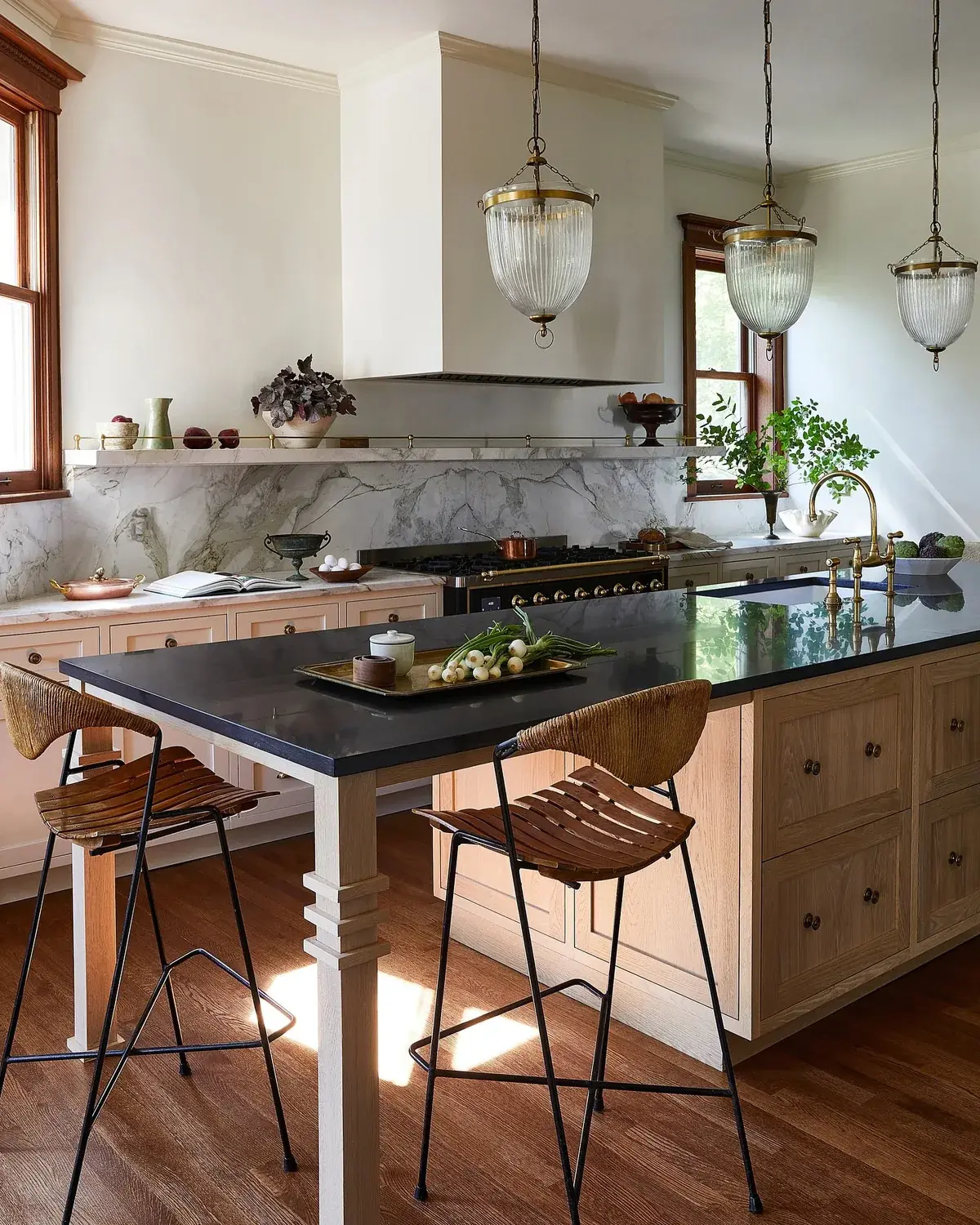 Black granite island with wicker and leather stools in a warm white kitchen