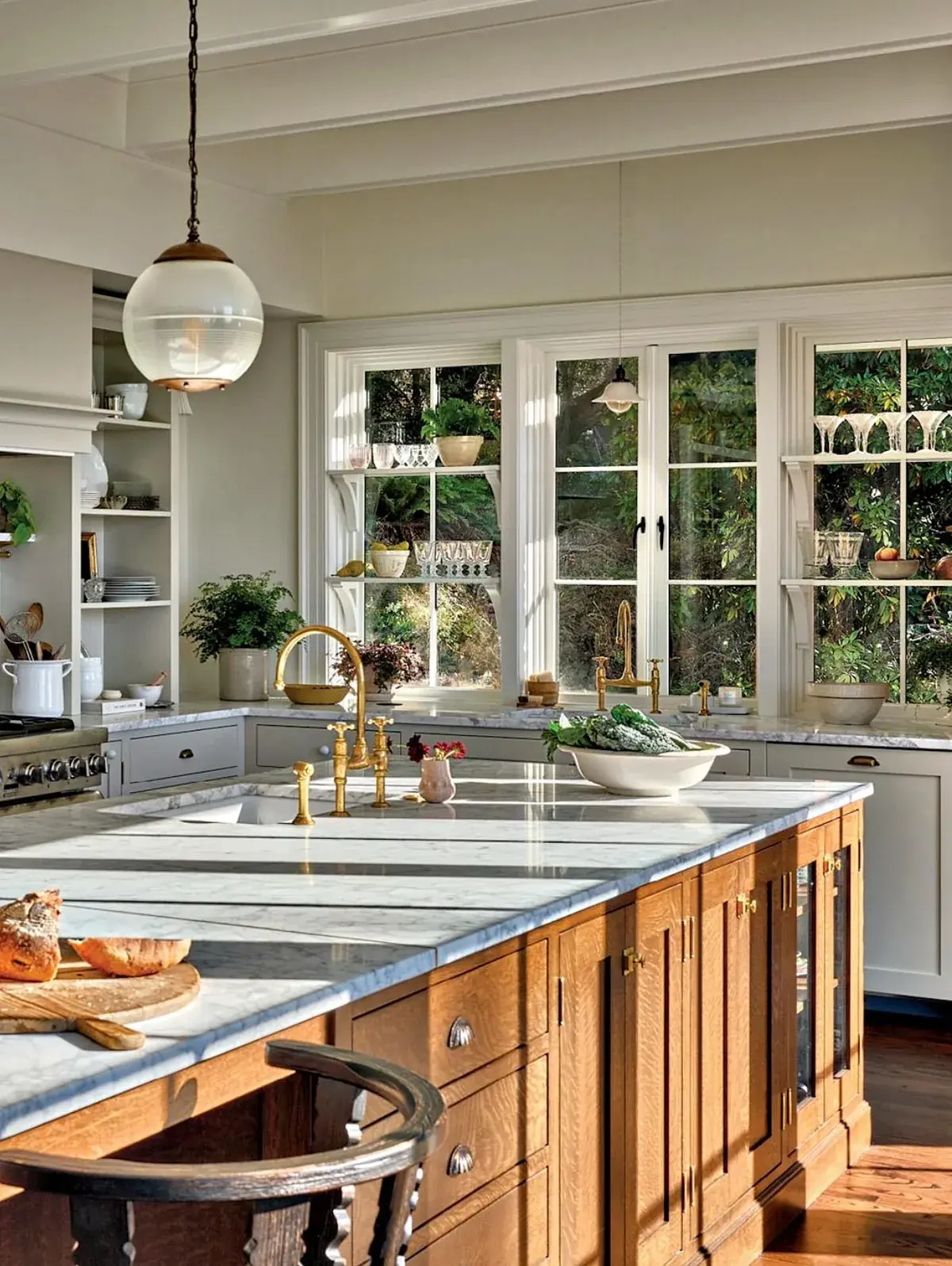 Oak island with a marble top in a white kitchen with garden windows