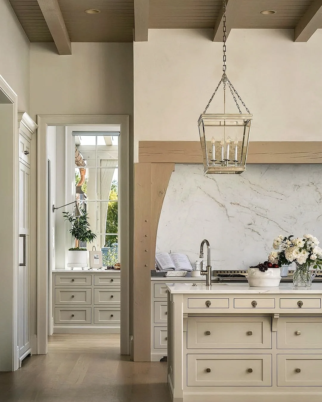 Cream island with a full height marble slab splashback framed in oak and a glass lantern above