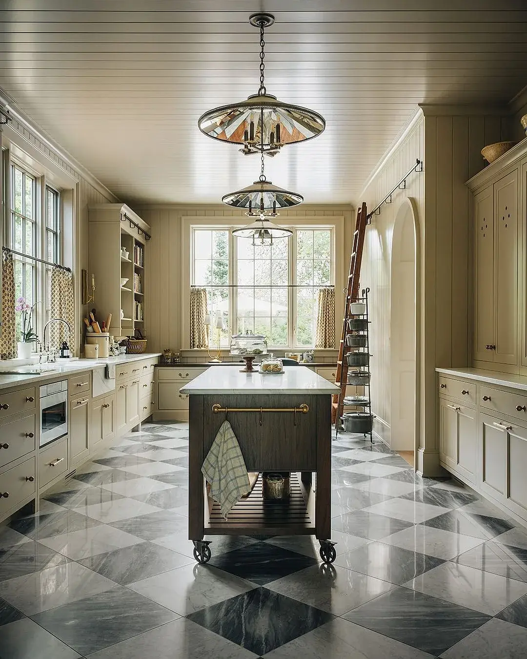 Galley kitchen with a polished chequered marble floor and a dark timber island on wheels