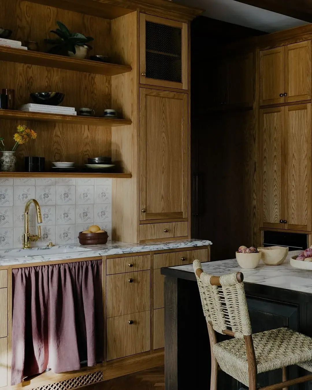Oak kitchen with a thin marble worktop, floral tile splashback and a mauve sink curtain