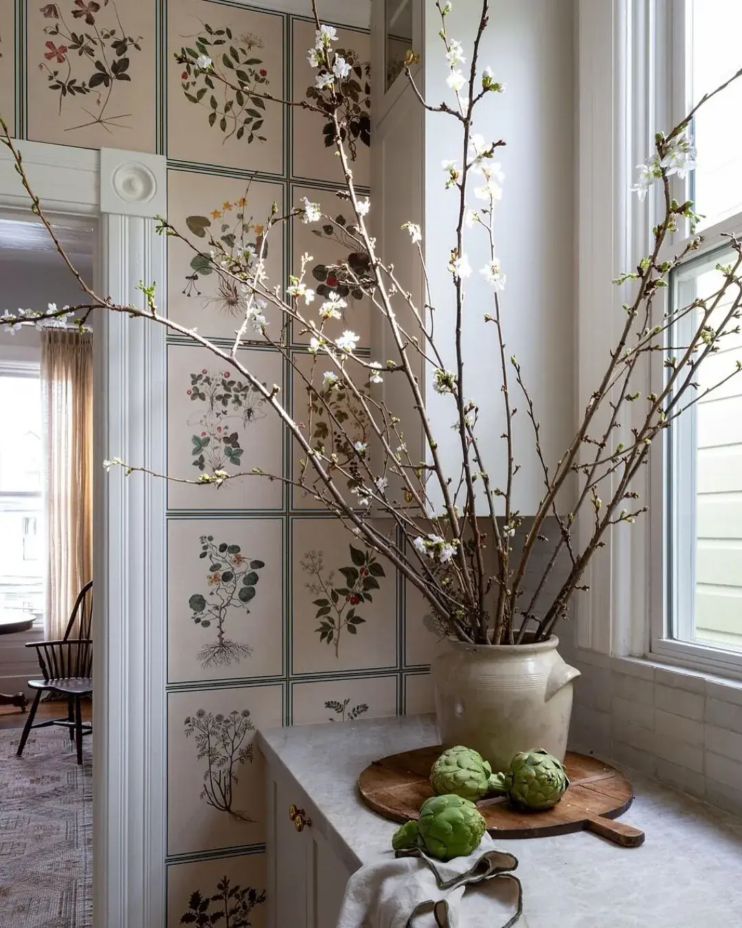 Small marble worktop corner with botanical panels, a stoneware crock and artichokes on a board