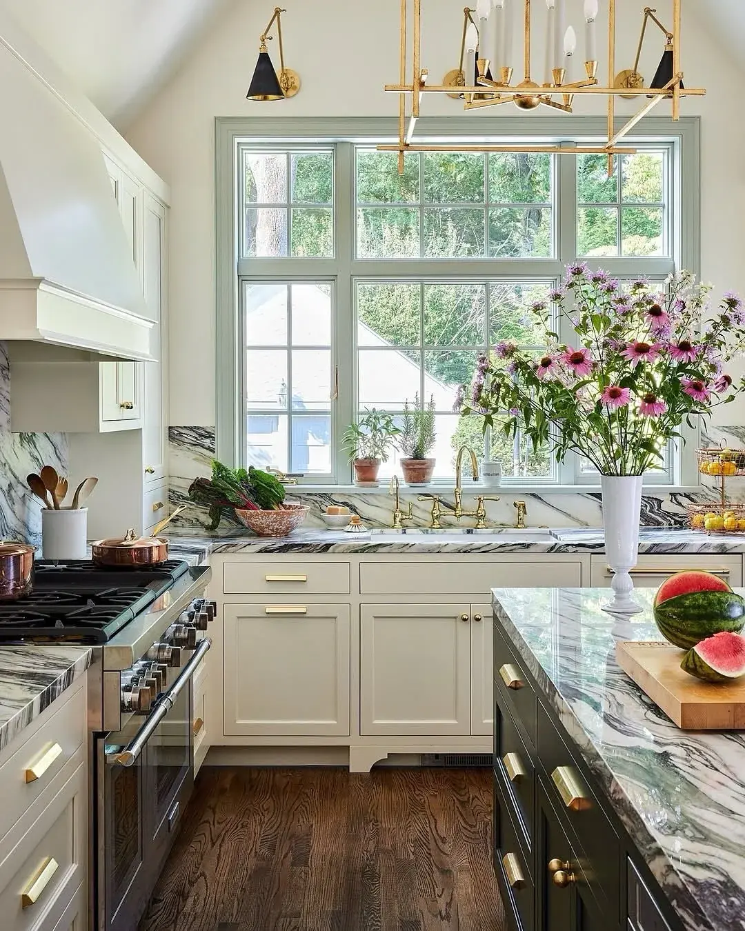 Kitchen with green veined marble worktops, cream cabinets, a dark green island and copper pans