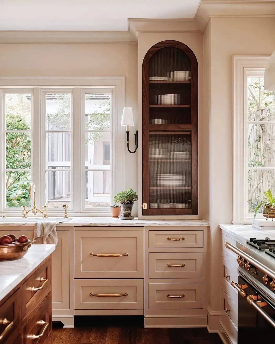 Tall arched walnut cabinet with reeded glass beside a kitchen window