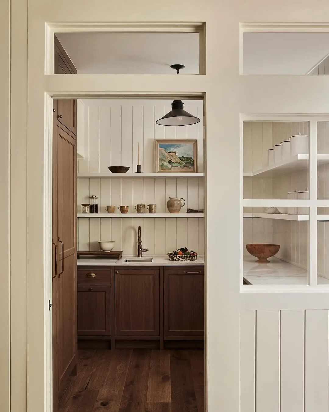 Small pantry with white open shelves and dark timber base units seen through a doorway