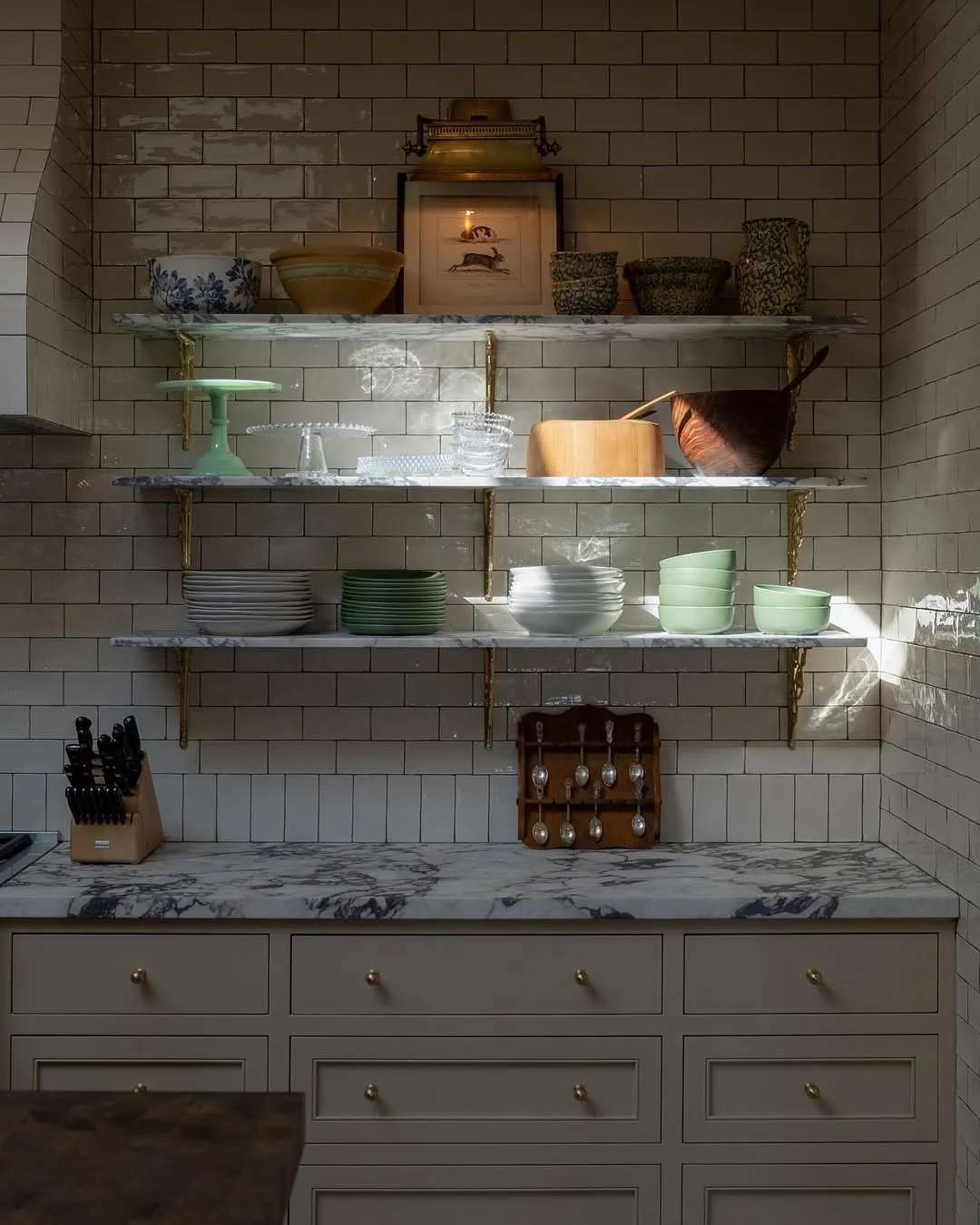 Three marble shelves on white subway tile with brass brackets and stacked bowls