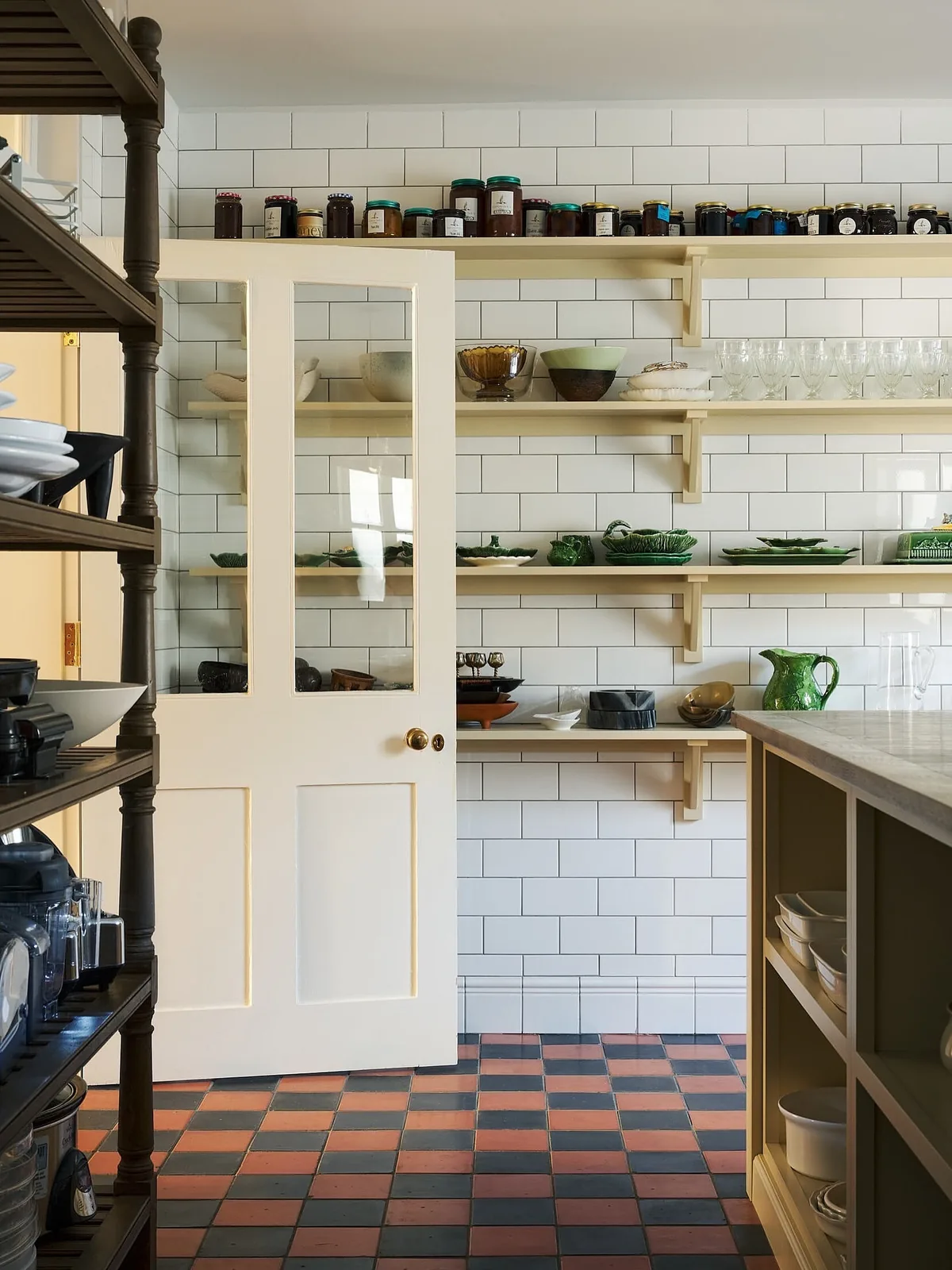 Walk-in pantry with cream shelves of green tableware and preserves above white tile