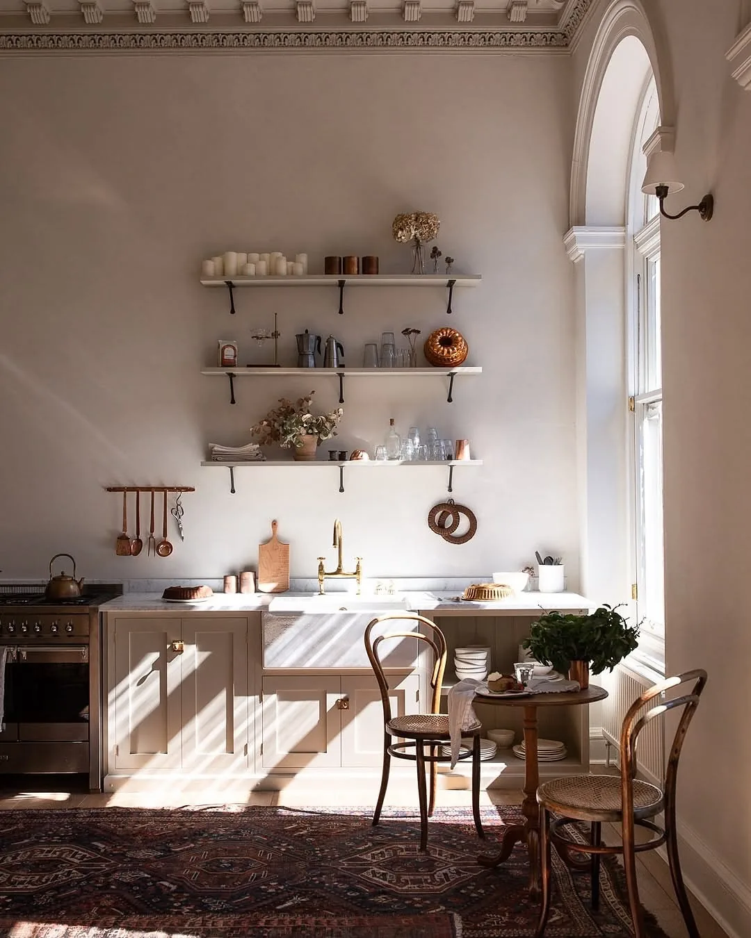 Tall white wall with three sparse shelves above a sink beside an arched window