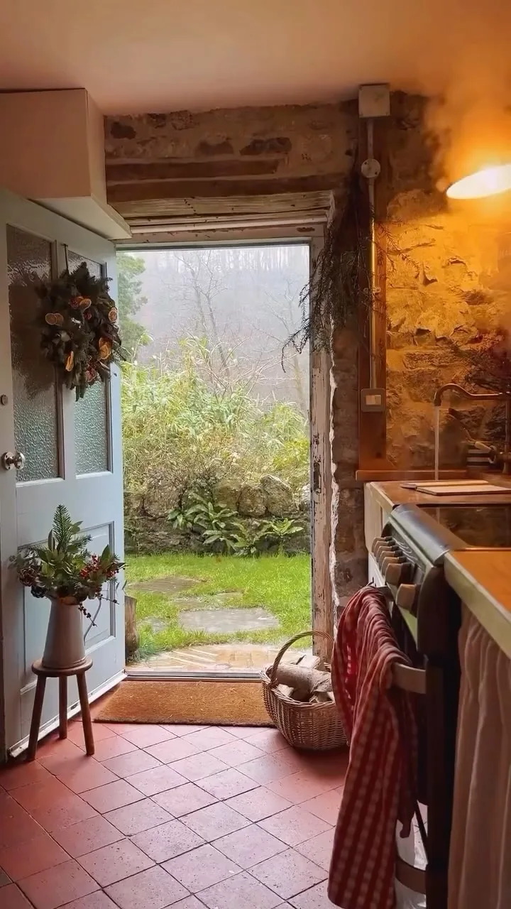 Cottage doorway with rough stone walls, a pale blue door, a cream range cooker and terracotta floor tiles
