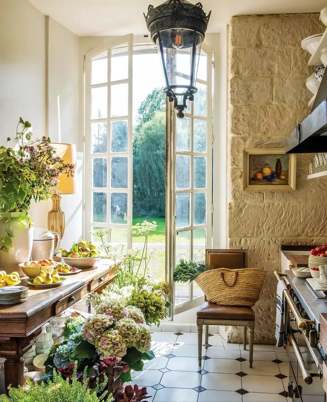 French country kitchen with cream joinery, a limestone wall, a black iron lantern and an octagonal tiled floor