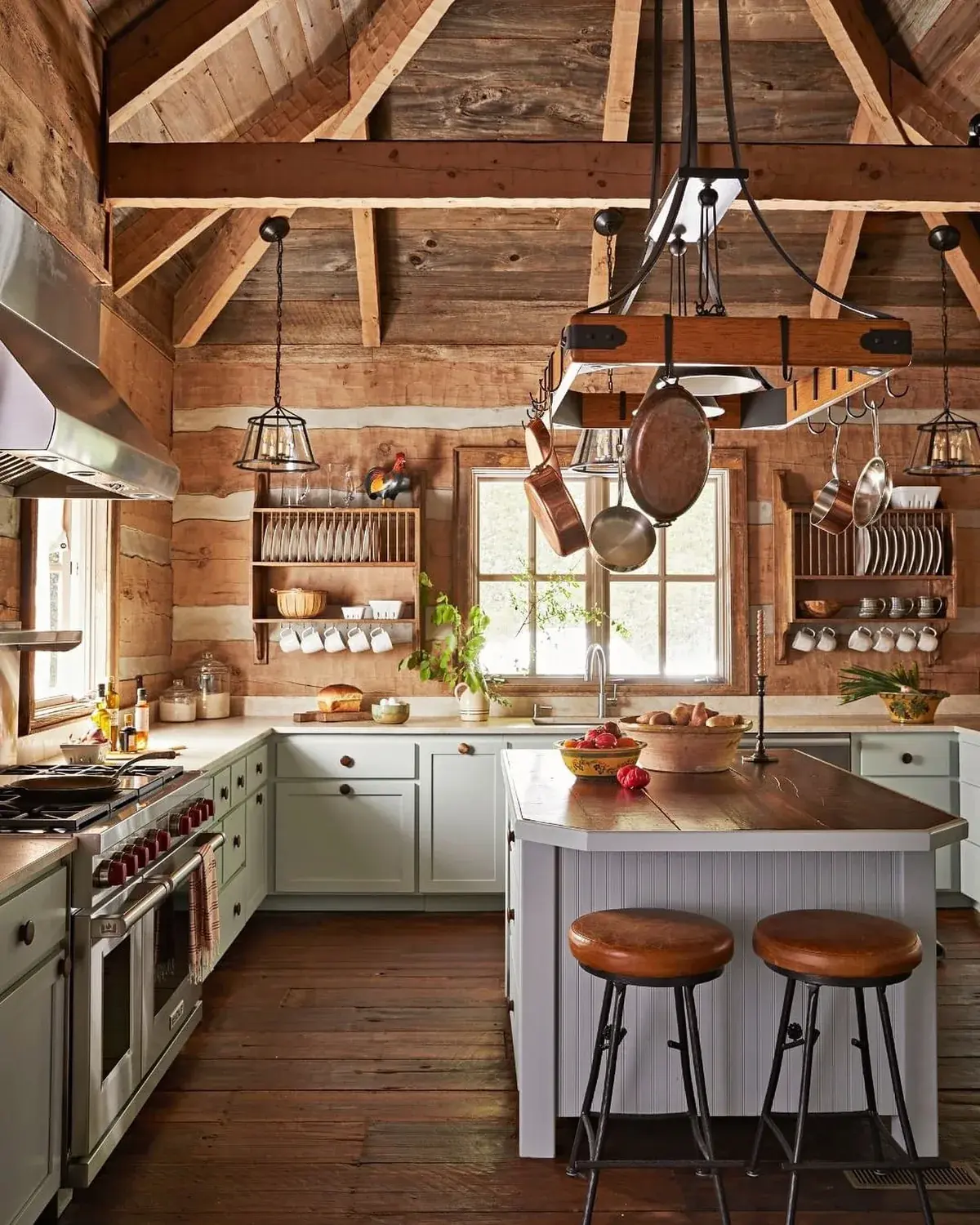 Log cabin kitchen with sage green painted cabinets, a grey-blue tongue and groove island and dark timber floor