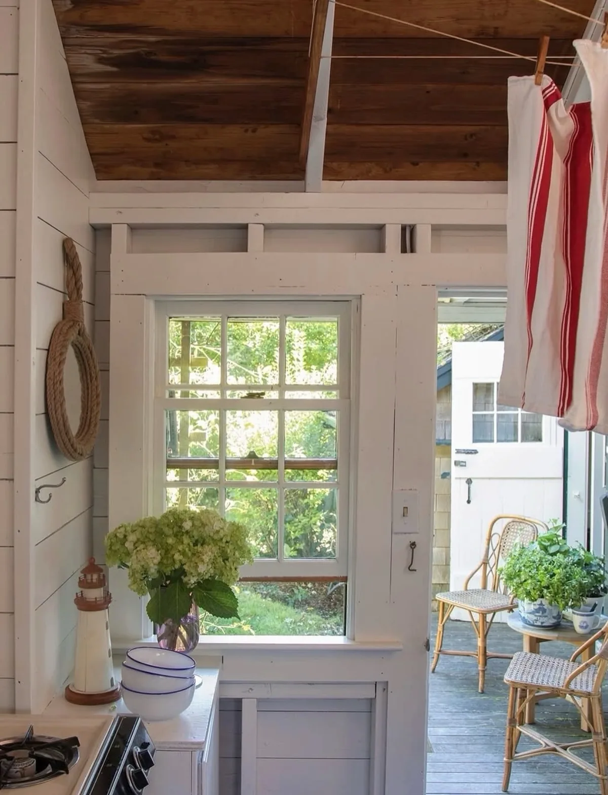 White shiplap cottage kitchen with a painted window frame, a dark stained ceiling and white china with blue rims