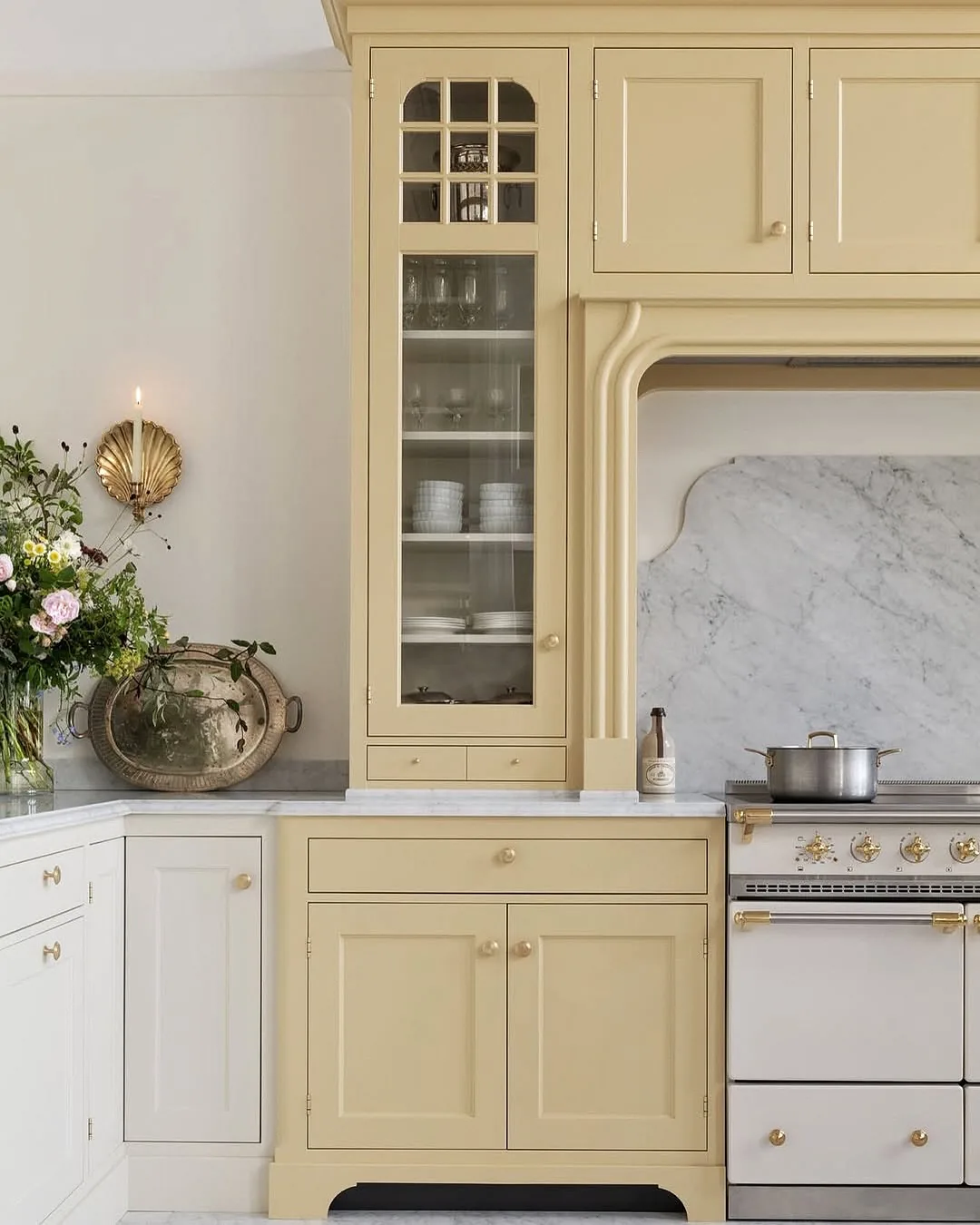 Butter yellow French country dresser with an arched range surround, brass knobs and a marble splashback