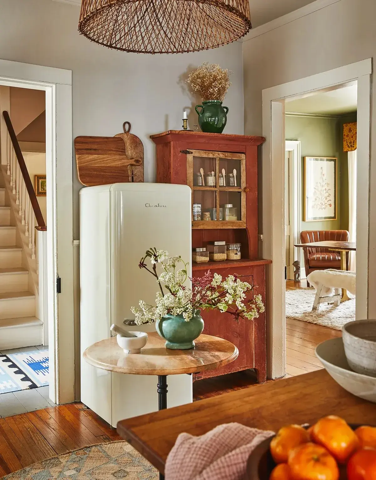 Cream retro fridge beside a red-painted pine cupboard with a round marble table in front