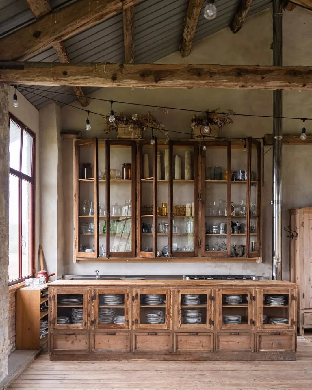 Barn kitchen with old glazed cabinets full of glassware above a long timber cabinet run