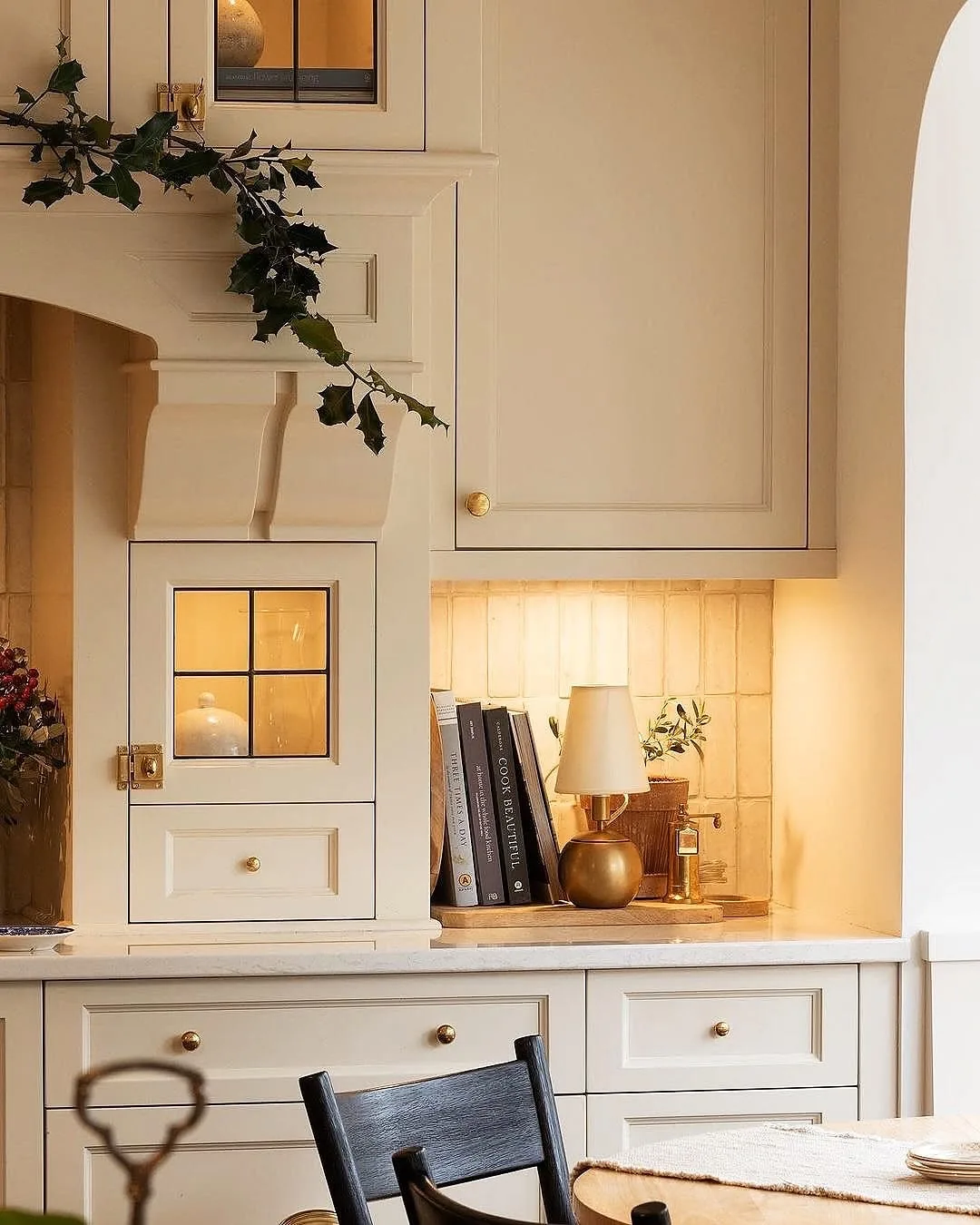 Cream alcove with a small brass lamp glowing, books and a leaded glass cupboard