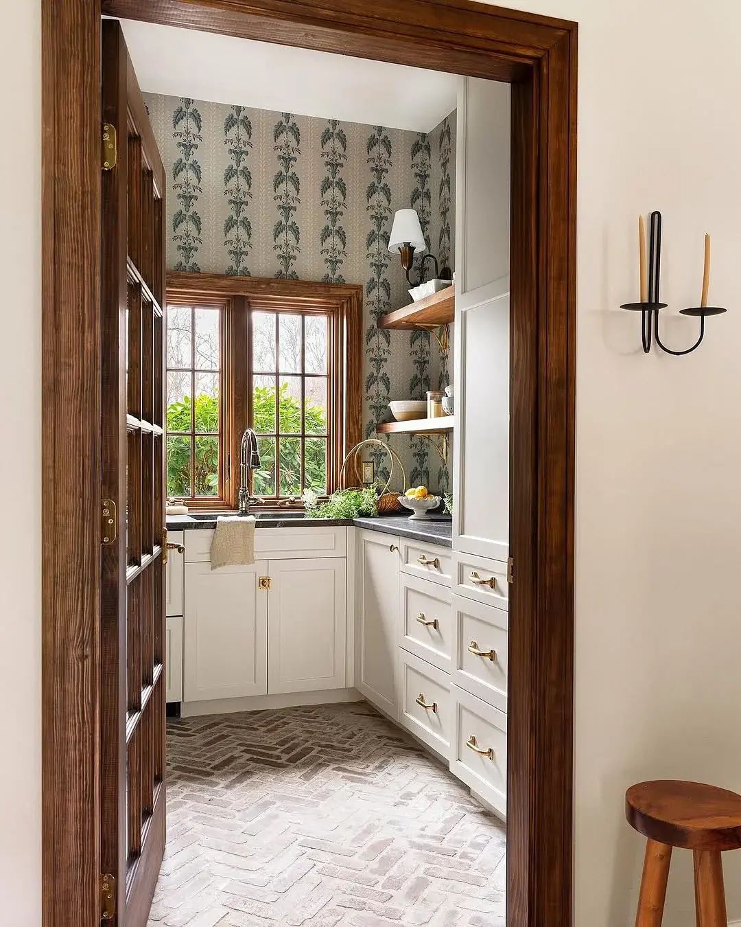 Scullery with botanical wallpaper, cream cabinets and a reclaimed brick herringbone floor
