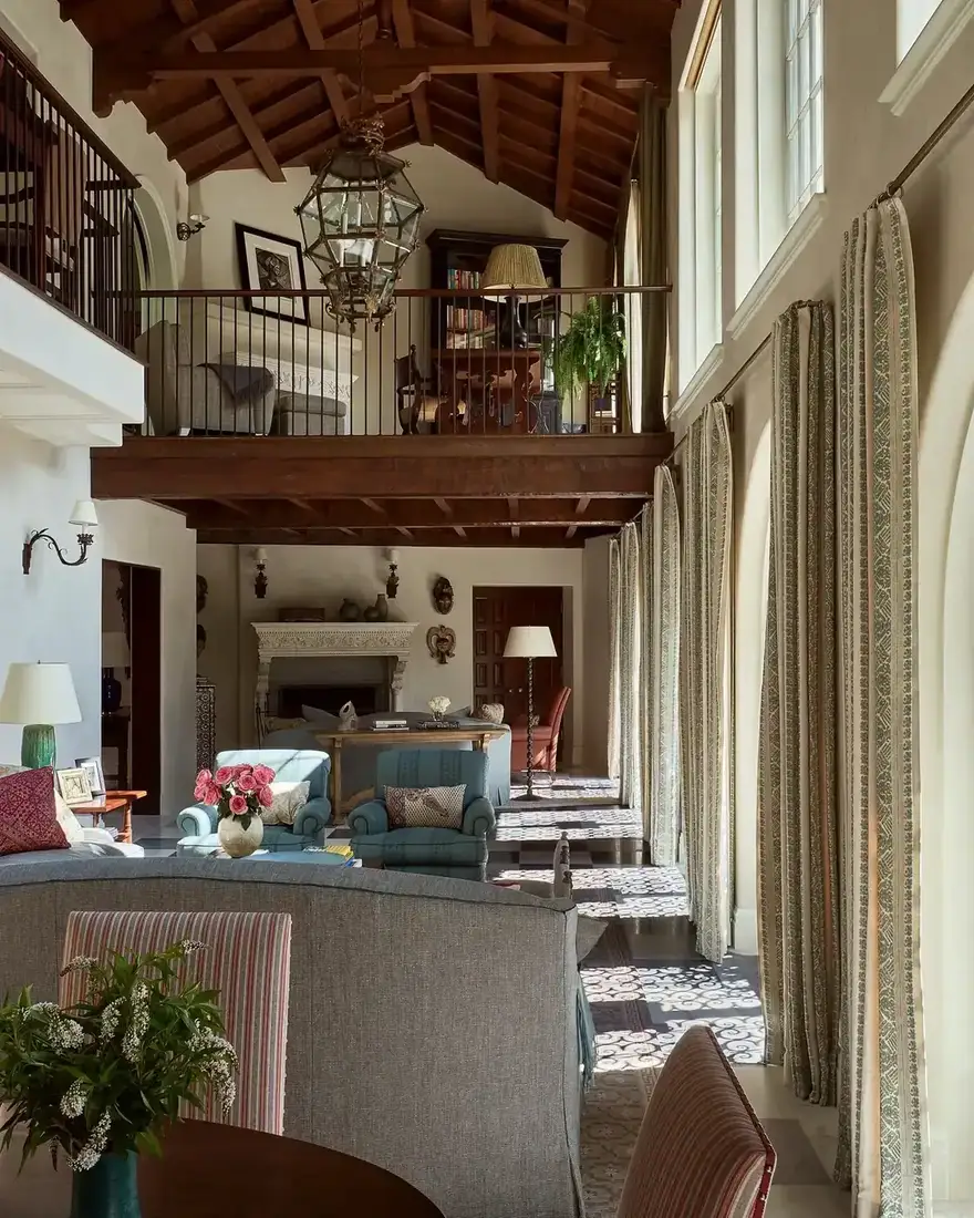 Double height living room with dark timber mezzanine, tall linen curtains and a hanging lantern