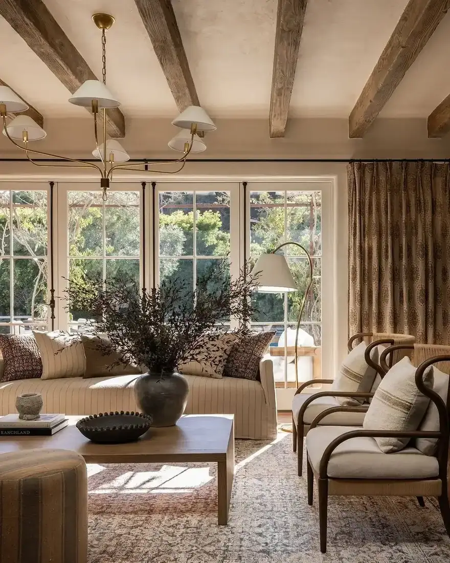 Sitting room with rough grey brown beams, striped linen sofa and brass six arm chandelier