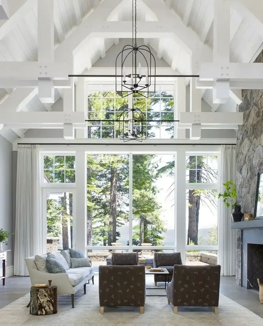 Tall white vaulted sitting room with painted trusses, stone fireplace and full height glazing