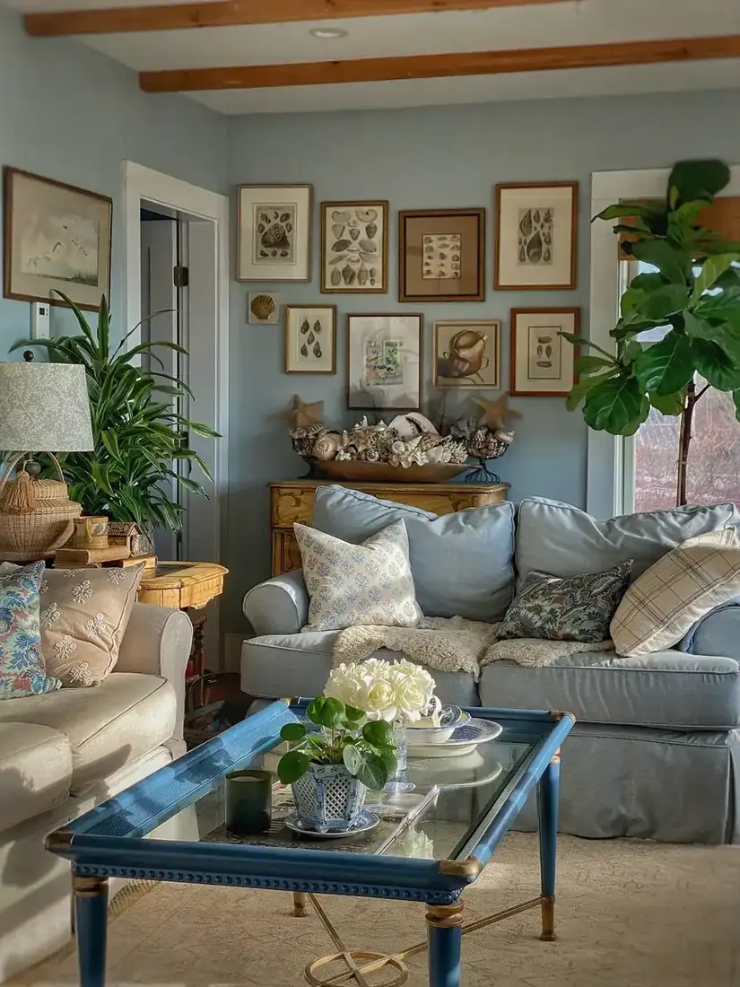 Pale blue living room with shell print gallery wall and blue glass table