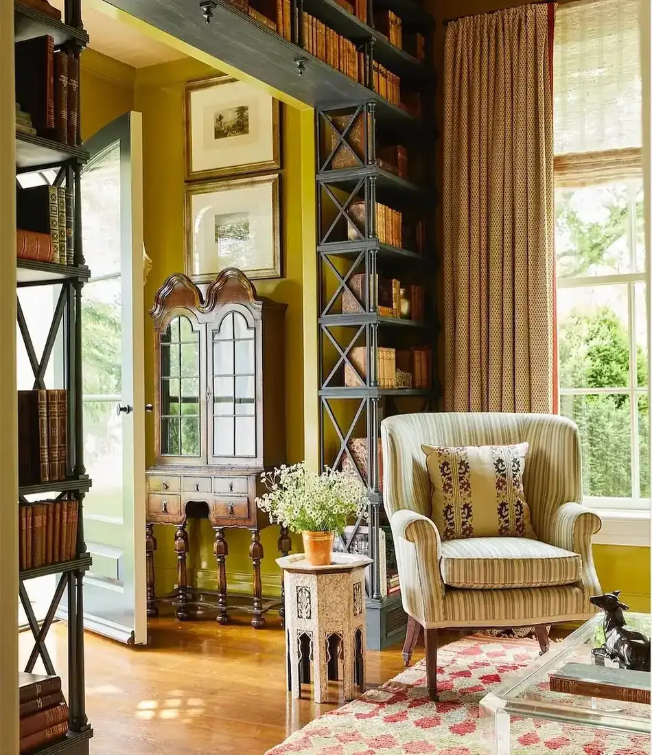Dark freestanding X-braced shelves with books and mustard walls beyond