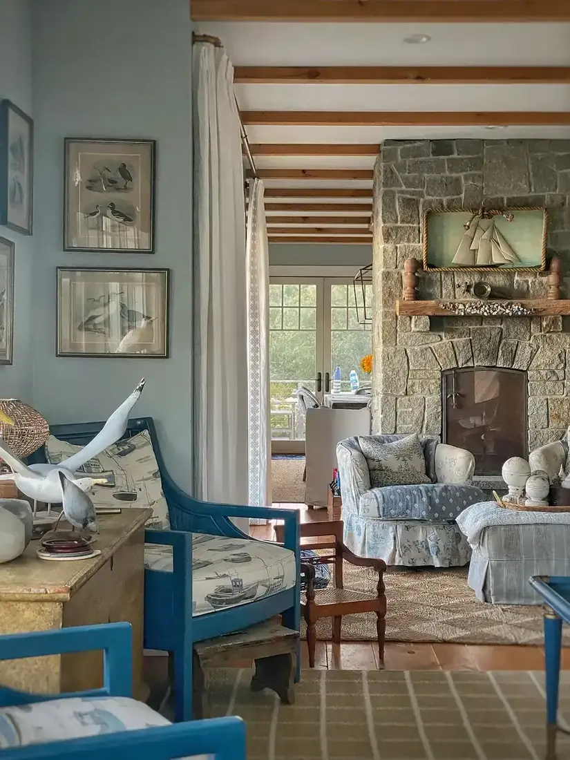 Stone fireplace with blue chairs, wooden chest and ship diorama above mantel