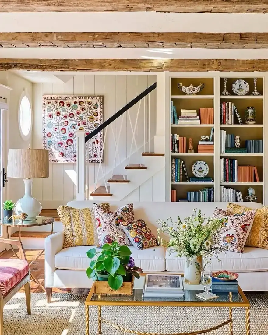 White sofa with colourful cushions, exposed beams and bookshelves beside stair