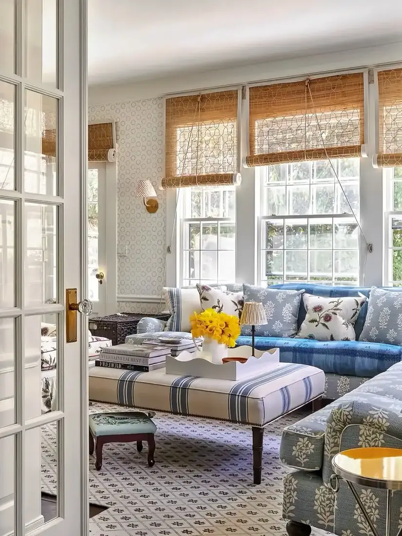 Blue patterned sofa with striped ottoman and woven blinds in a bright sitting room